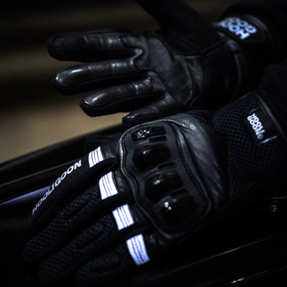 Close-up of a gloved hand on a motorcycle handlebar with illuminated buttons.