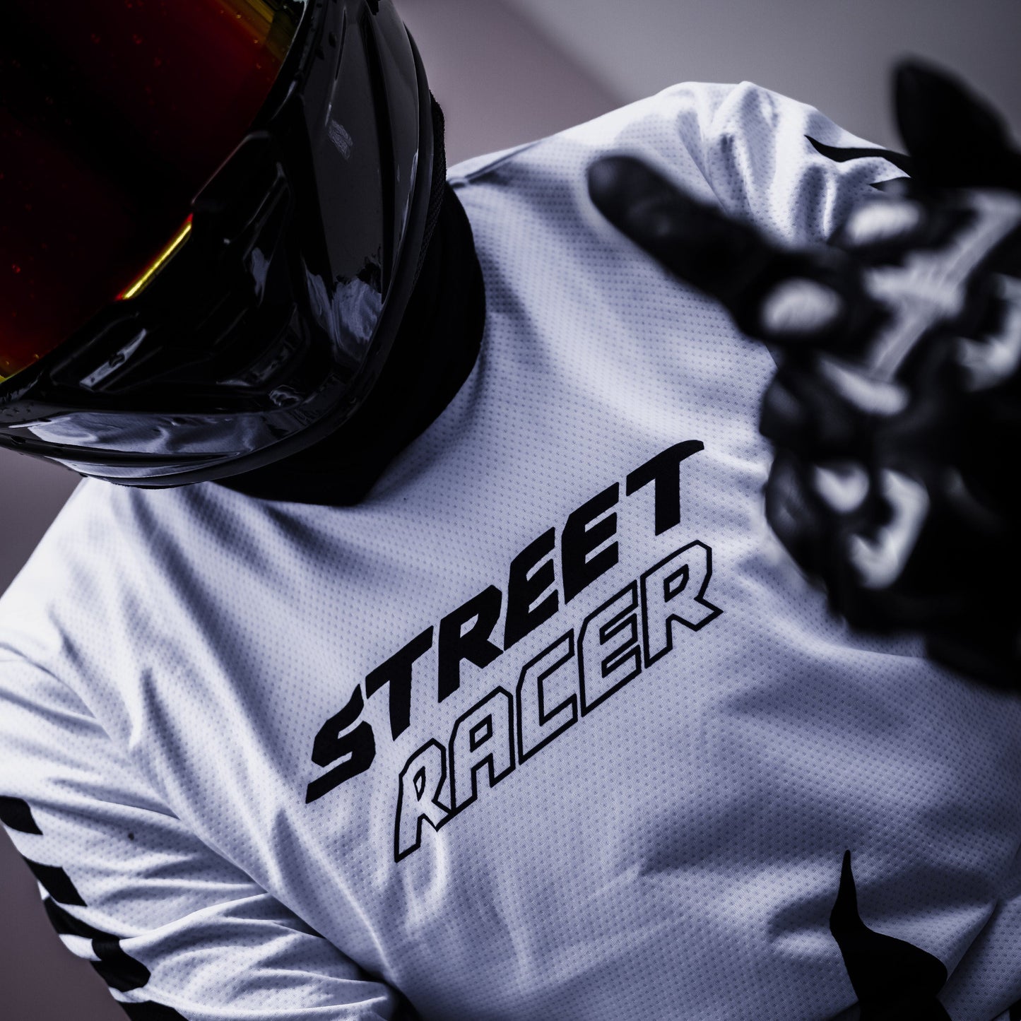 Person wearing a white long-sleeve shirt with 'Street Racer' text, black gloves, and helmet on a dark background