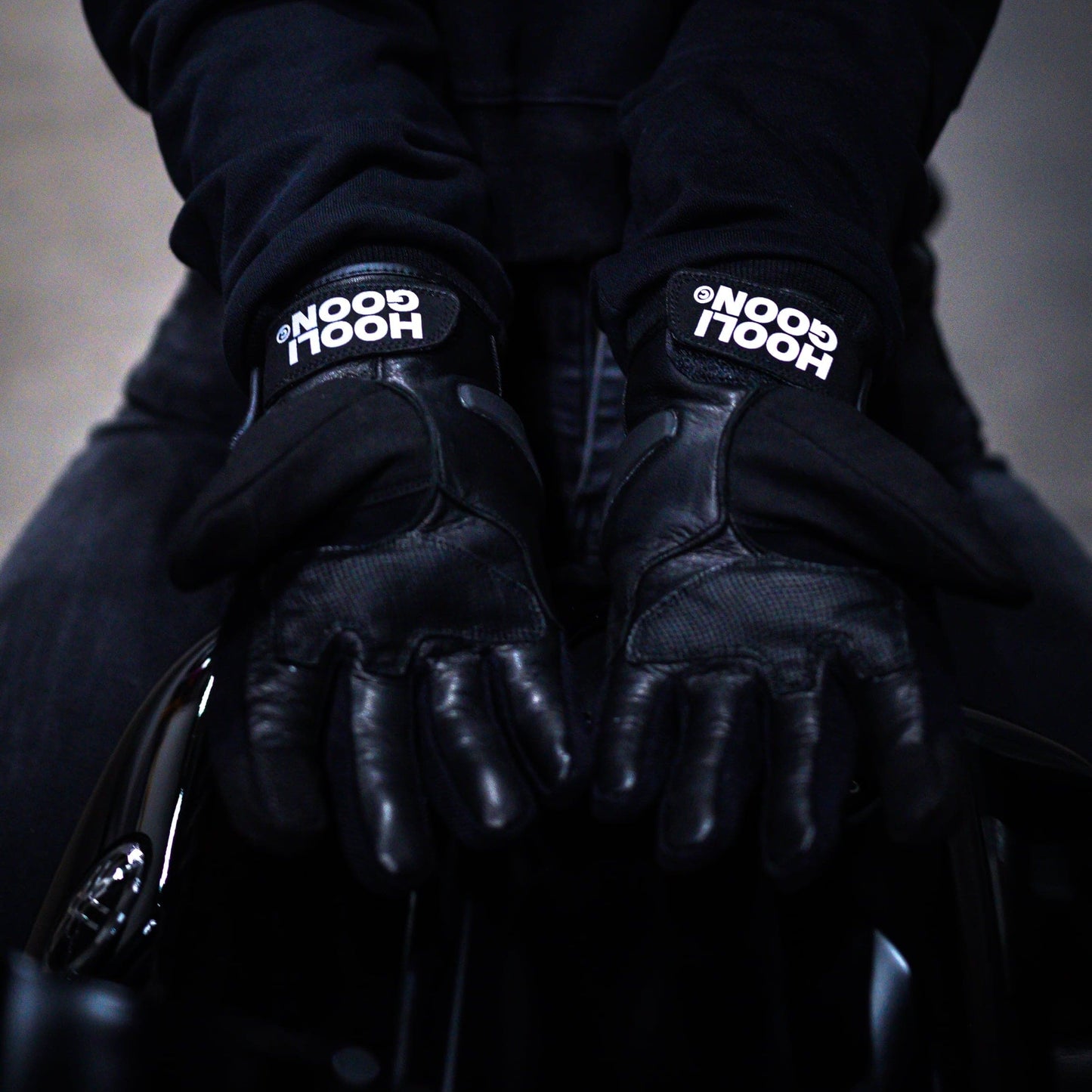 Person wearing a black hoodie and gloves with 'HOOLIGOON' branding on a dark background
