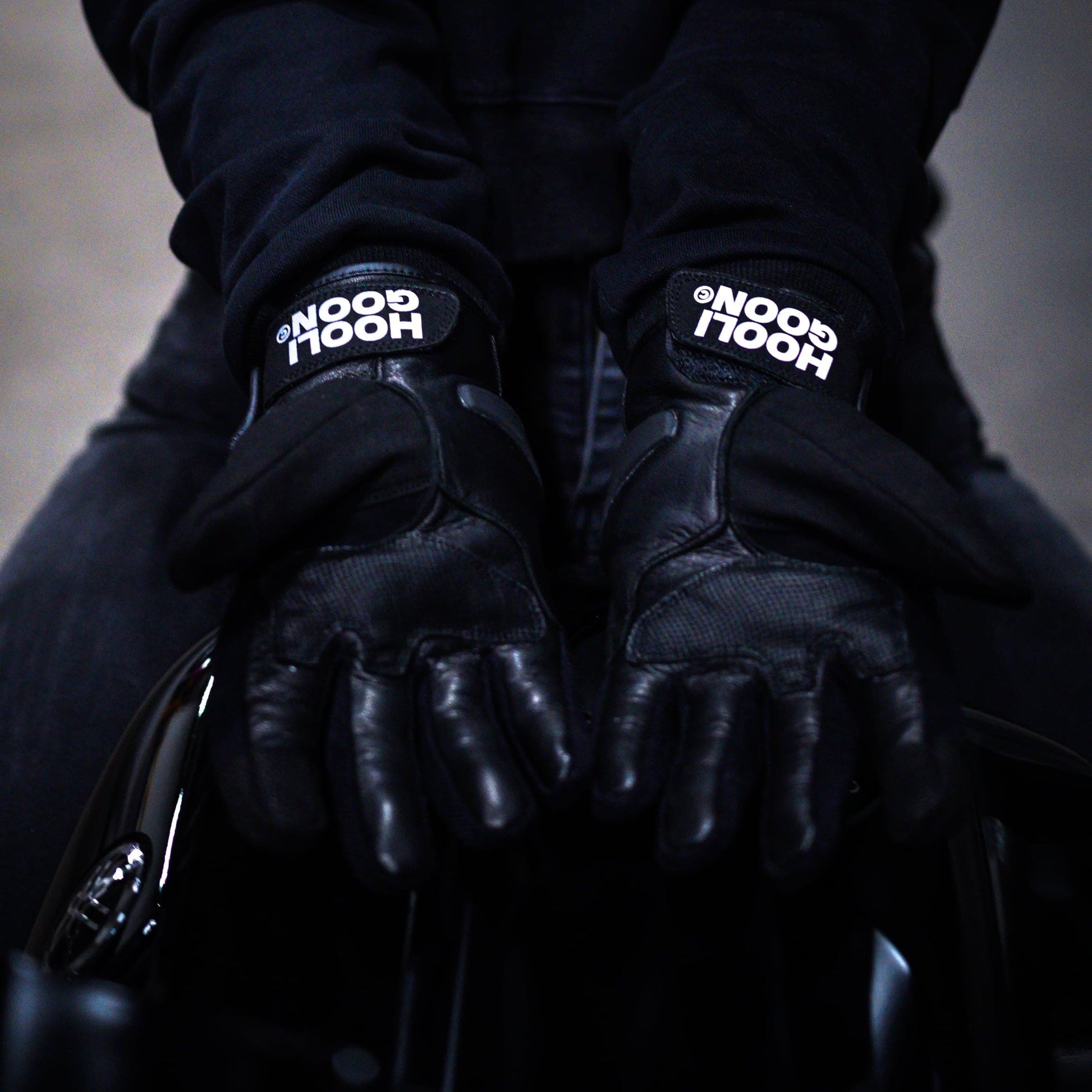 Person wearing a black hoodie and gloves with 'HOOLIGOON' branding on a dark background
